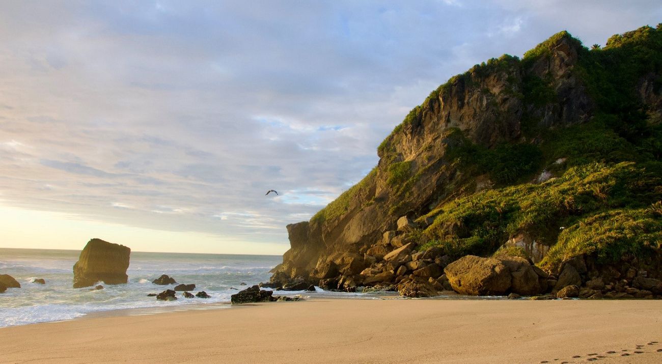 A sandy beach meets up with a rock outcrop next to the ocean.