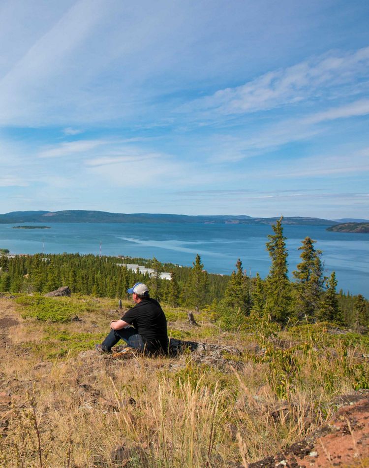 A person sits on a cliff overlooking water.