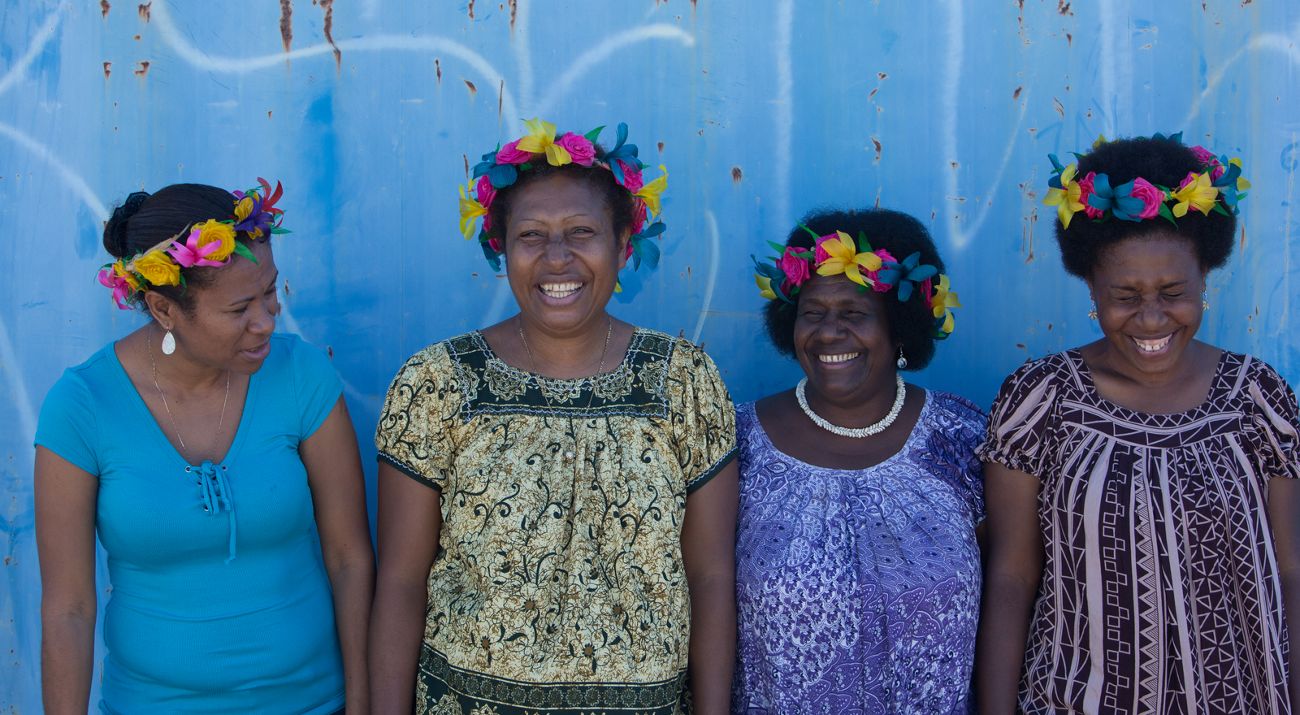 Four Pacific women smiling against a blue background.