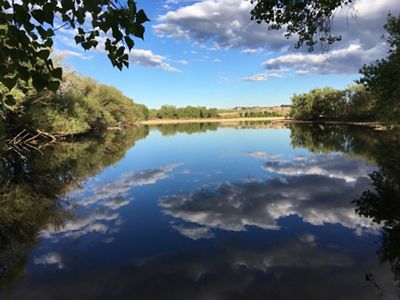 Blue sky and white clouds reflected in the waters of a placid lake.